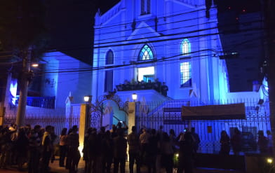 Foto do lado de fora da igreja mostrando toda sua fachada durante a noite com luzes azuis iluminando a igreja