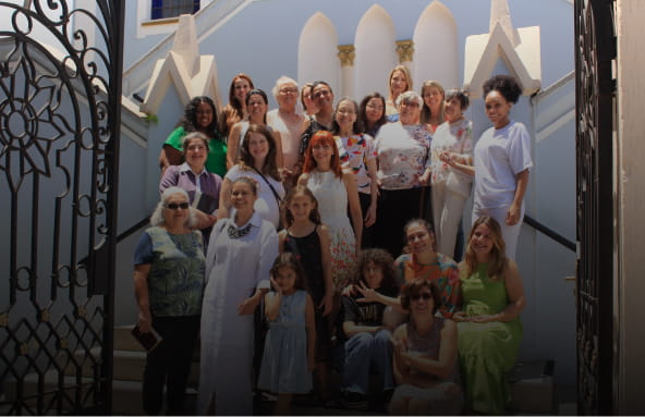 Grupo de mulheres sorrindo reunidas em uma escada em frente a igreja